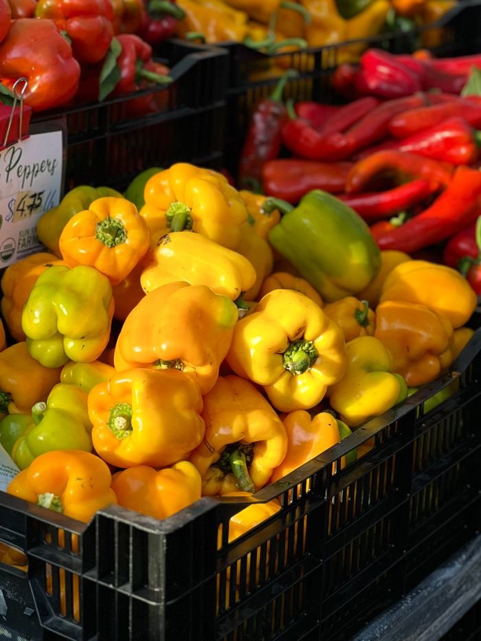Colorful yellow and green bell peppers stacked in black crates at a farmer's market.