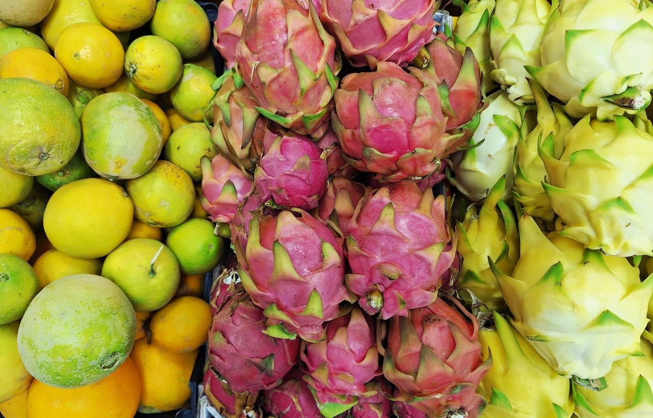 Colorful display of dragon fruits and citrus at a market, showing tropical freshness.